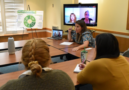 Three therapists in a meeting with two therapists joining in virtually on a large screen in the background